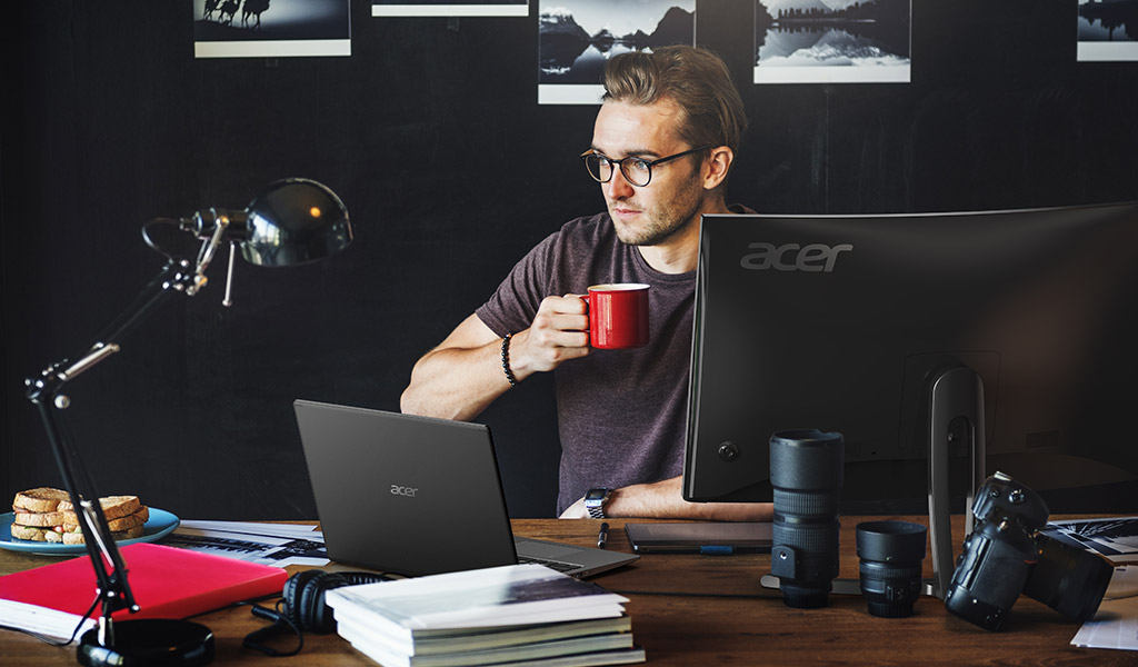 Man sitting at desk with an Acer laptop connected to large Acer desktop Monitor